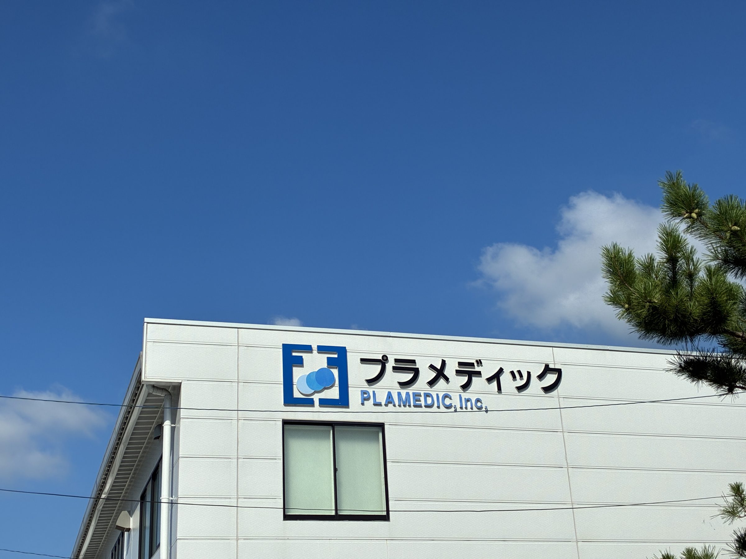 青空を背景にした有限会社プラメディックの本社社屋と社名サイン